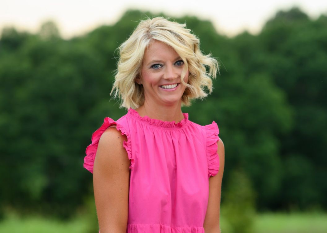 Angela wears a bright pink blouse and smiles for a photo outside.